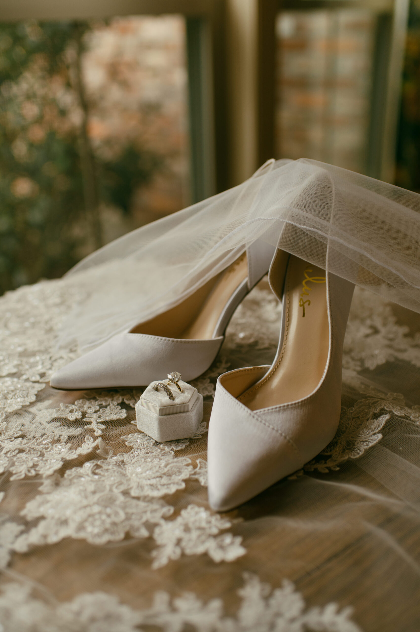 A bride's shoes lay with her tulle gloves, wedding rings and veil during a details flat lay.