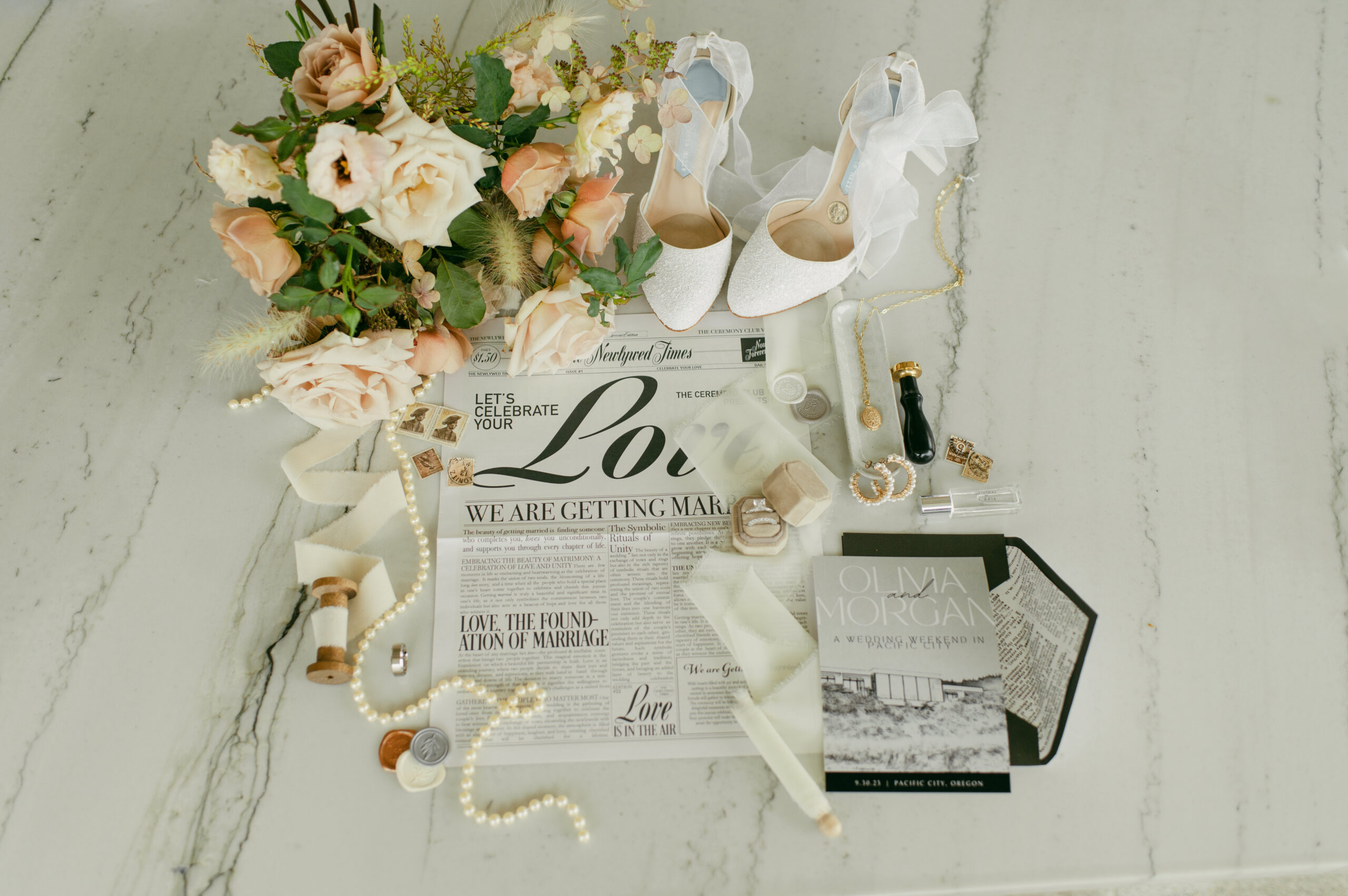 a wedding details shot with wedding shoes, invitation suite, newspaper, flowers and jewelry.