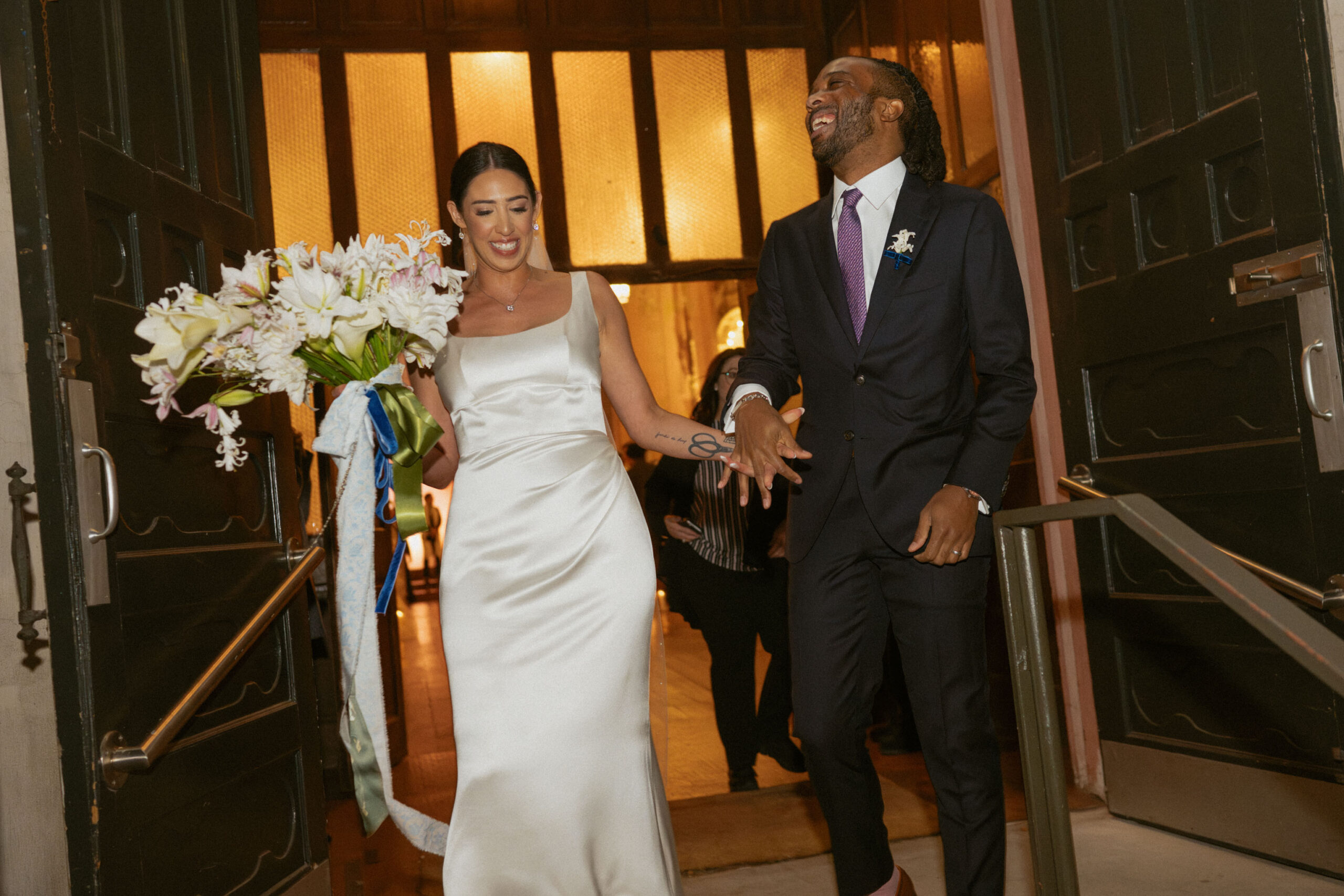 Newlyweds exiting City Hall after their marriage ceremony, holding hands and celebrating.